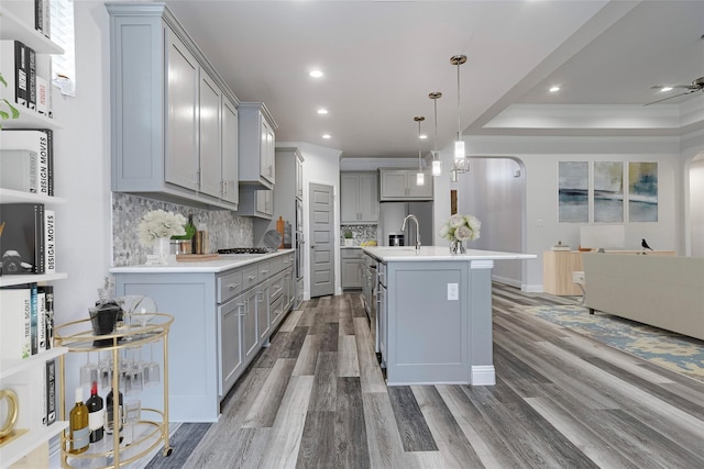 kitchen with arched walkways, an island with sink, decorative light fixtures, gray cabinets, and light countertops