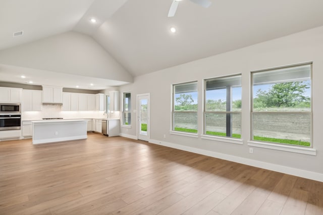 unfurnished living room featuring high vaulted ceiling, light wood-type flooring, a healthy amount of sunlight, and baseboards