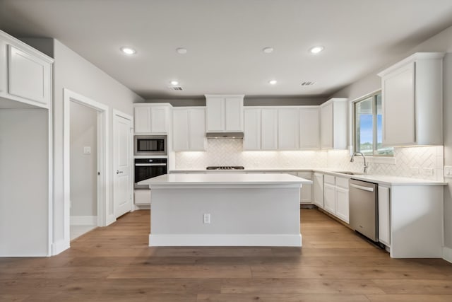 kitchen featuring a kitchen island, appliances with stainless steel finishes, light countertops, white cabinetry, and a sink