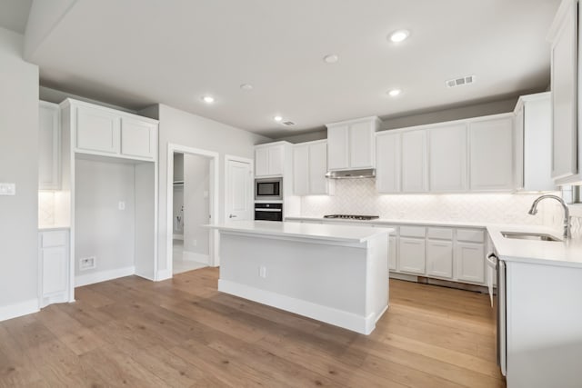 kitchen with a sink, white cabinets, light countertops, appliances with stainless steel finishes, and a center island