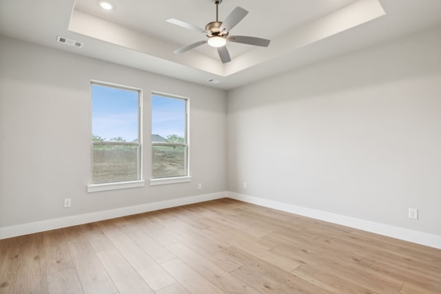 unfurnished room featuring a tray ceiling, baseboards, visible vents, and light wood finished floors