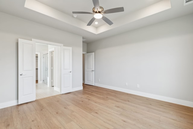 unfurnished bedroom featuring a raised ceiling, visible vents, light wood-style flooring, a ceiling fan, and baseboards