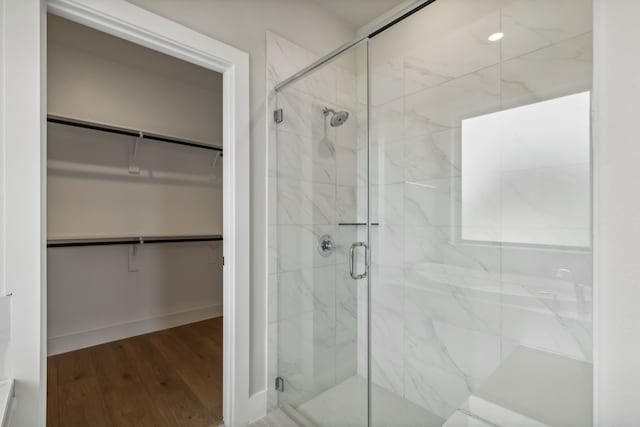 full bath with a walk in closet, a shower stall, and wood finished floors