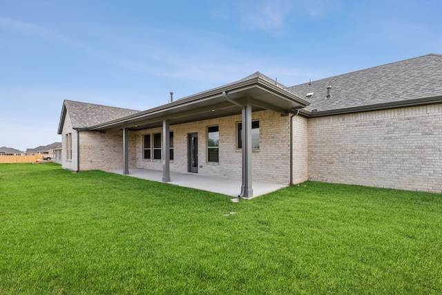 rear view of property with roof with shingles, a patio, brick siding, and a lawn