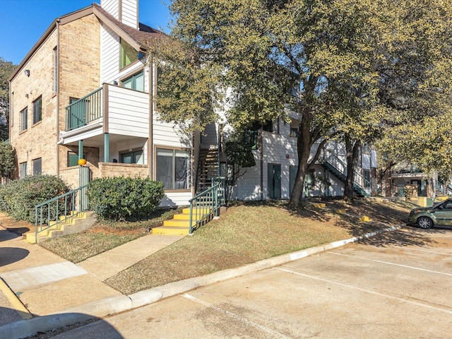 view of property featuring stairs, uncovered parking, brick siding, and a chimney