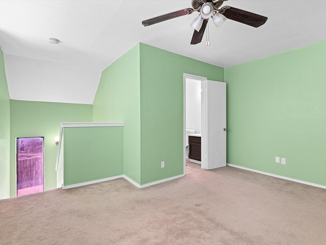 interior space featuring ceiling fan, connected bathroom, light carpet, baseboards, and vaulted ceiling