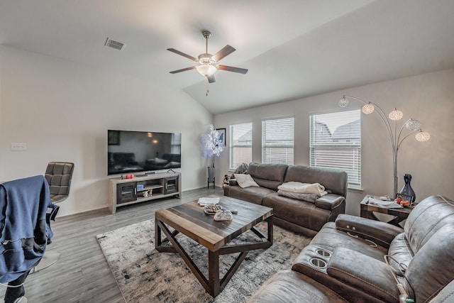 living area with visible vents, baseboards, ceiling fan, light wood-style flooring, and vaulted ceiling