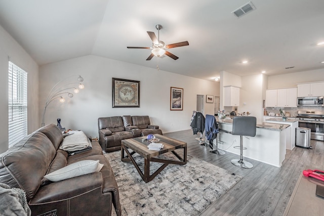 living room with vaulted ceiling, a ceiling fan, visible vents, and light wood-style floors