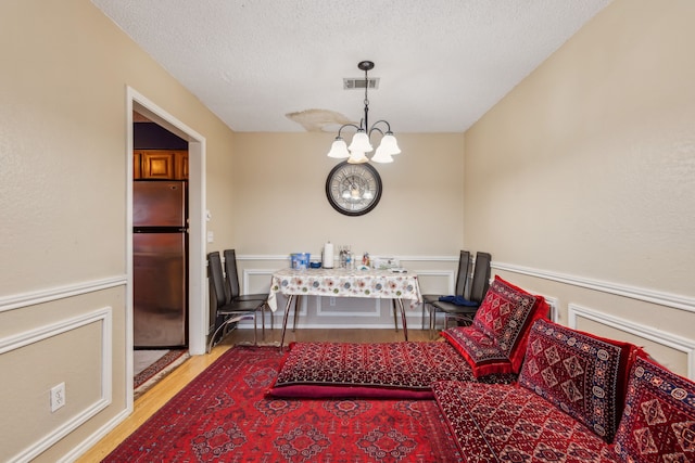 dining room featuring visible vents, an inviting chandelier, light wood-style floors, wainscoting, and a textured ceiling