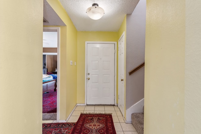 foyer featuring stairs, a textured ceiling, baseboards, and light tile patterned floors