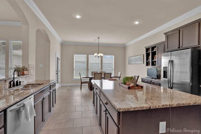 kitchen featuring light stone counters, hanging light fixtures, appliances with stainless steel finishes, dark brown cabinetry, and a sink