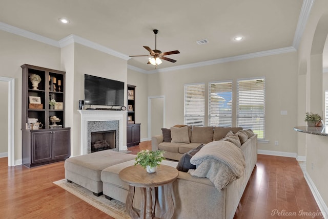 living room featuring light wood-style flooring, a fireplace, visible vents, and ornamental molding