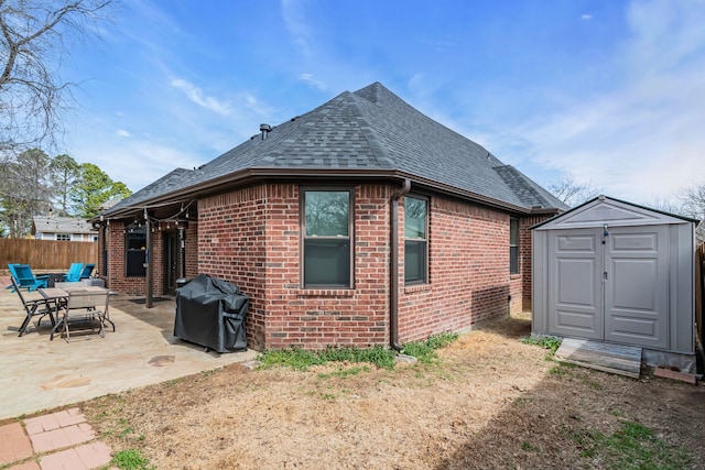 back of house with brick siding, a patio area, a storage unit, and roof with shingles