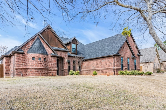 tudor house featuring a shingled roof, a front yard, and brick siding