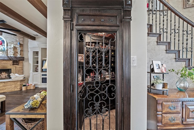 wine area with a stone fireplace, beamed ceiling, and wood finished floors