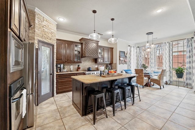 kitchen featuring stainless steel appliances, light countertops, hanging light fixtures, glass insert cabinets, and an island with sink