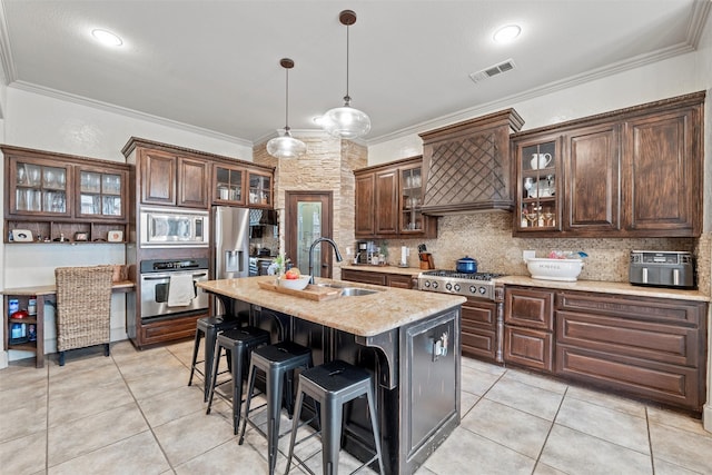 kitchen with visible vents, appliances with stainless steel finishes, glass insert cabinets, a kitchen island with sink, and a sink