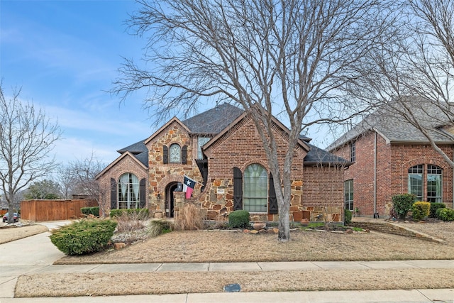 view of front of property with stone siding, a shingled roof, fence, and brick siding