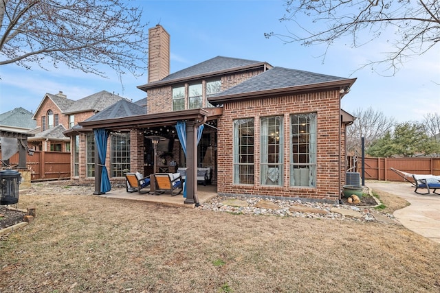 back of property featuring a fenced backyard, brick siding, roof with shingles, a chimney, and a patio area