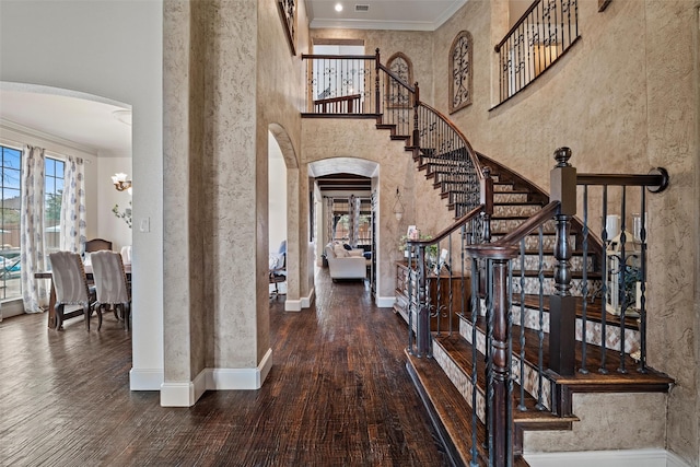 foyer featuring arched walkways, wood finished floors, a towering ceiling, baseboards, and crown molding