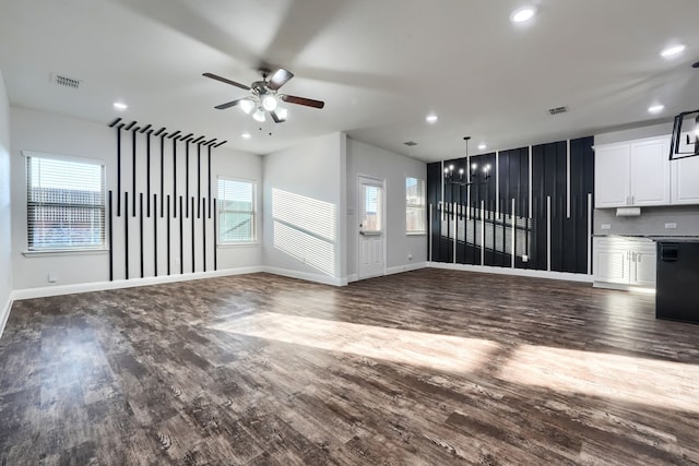 unfurnished living room with recessed lighting, ceiling fan with notable chandelier, visible vents, baseboards, and dark wood-style floors