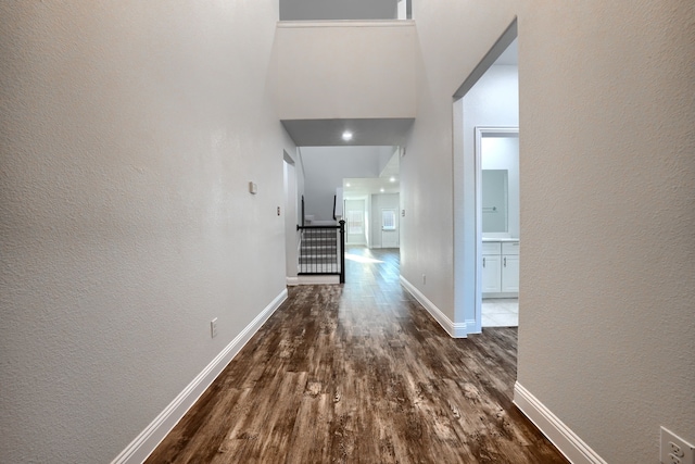 hall with dark wood-style floors, a textured wall, a towering ceiling, and baseboards