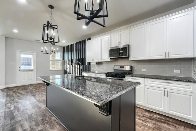 kitchen featuring a center island with sink, white cabinetry, stainless steel appliances, and dark stone counters