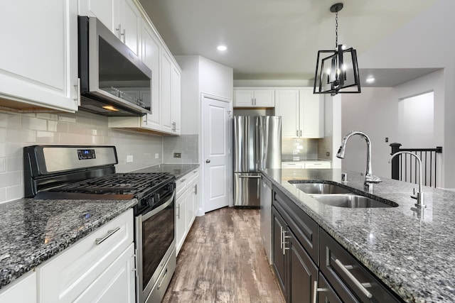 kitchen with white cabinets, dark stone countertops, stainless steel appliances, pendant lighting, and a sink