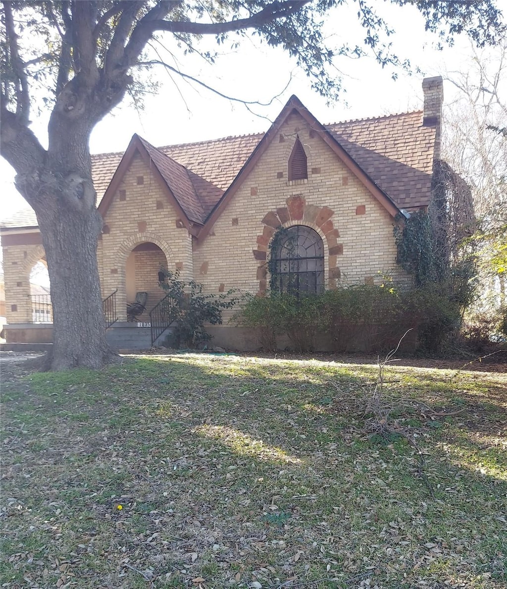 tudor-style house with a front yard, brick siding, and a chimney