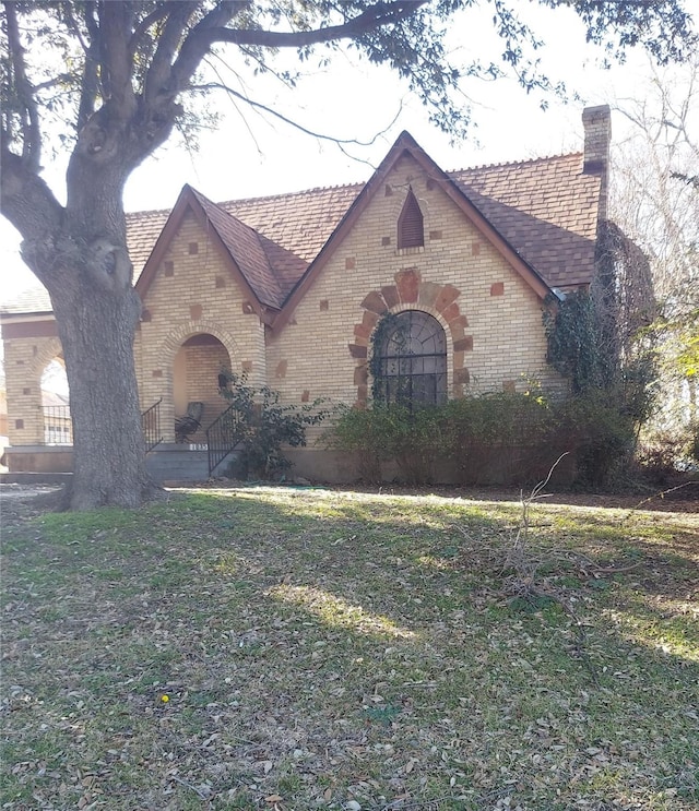 tudor-style house with a front yard, brick siding, and a chimney