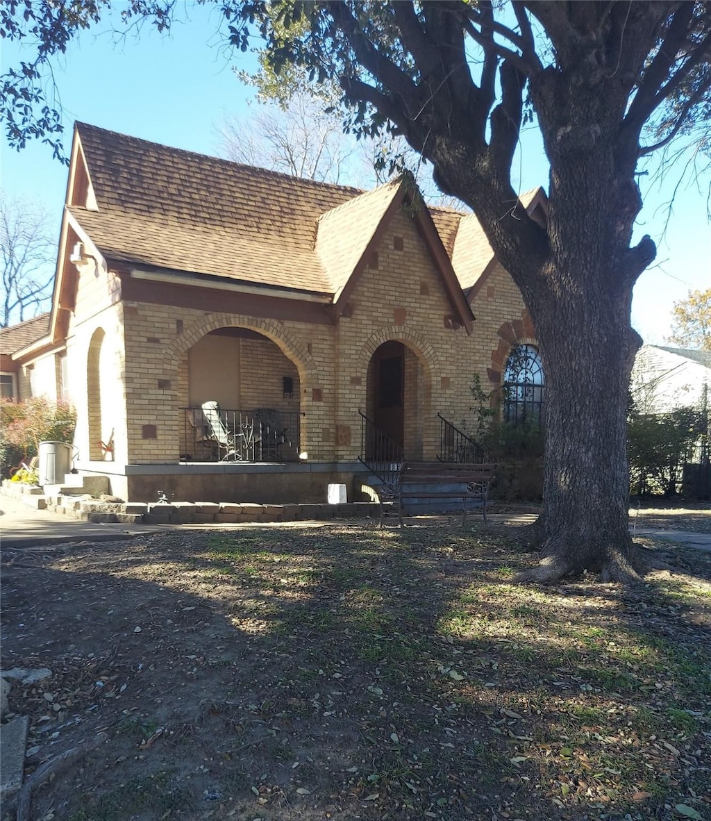 tudor home featuring brick siding, roof with shingles, and a porch