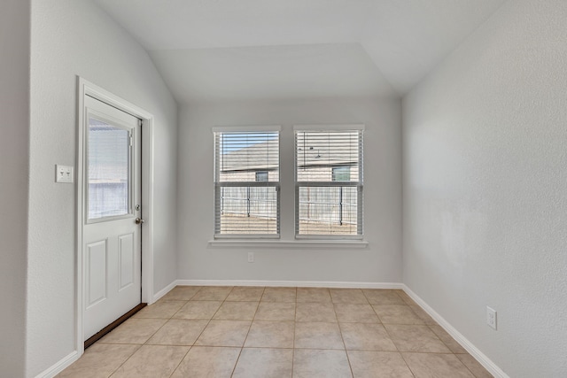 empty room featuring light tile patterned floors, baseboards, and vaulted ceiling