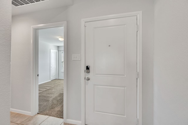 interior space featuring baseboards, light tile patterned floors, visible vents, and light colored carpet