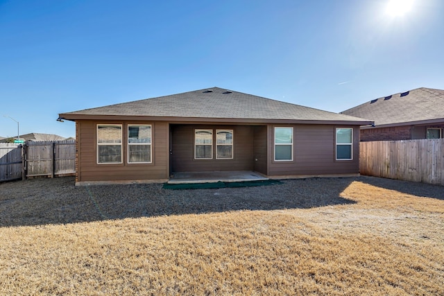 back of property with a patio, roof with shingles, and a fenced backyard