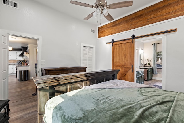 bedroom with wood finished floors, visible vents, ceiling fan, and a barn door