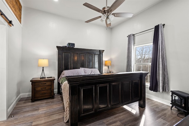 bedroom featuring dark wood-style floors, a barn door, a ceiling fan, and baseboards