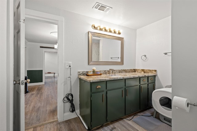 bathroom featuring wood finished floors, vanity, baseboards, visible vents, and crown molding