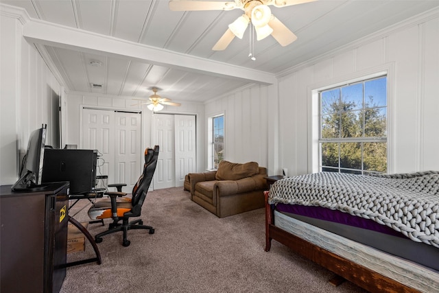 carpeted bedroom featuring ceiling fan, beamed ceiling, crown molding, a decorative wall, and two closets