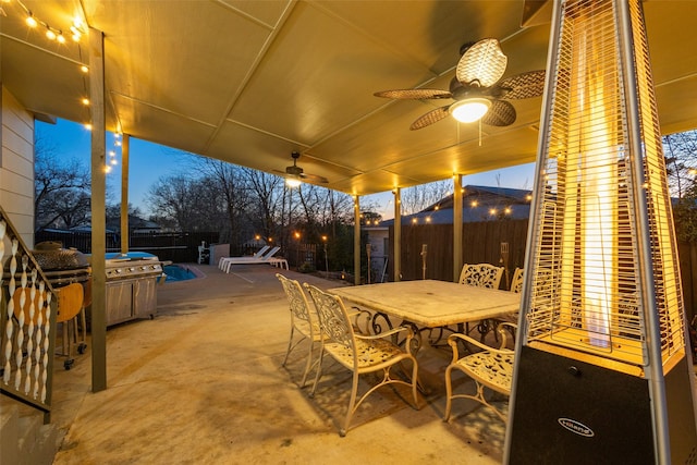 patio terrace at dusk featuring outdoor dining space, a fenced backyard, and a ceiling fan