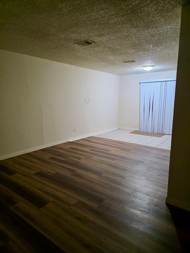 empty room featuring visible vents, a textured ceiling, baseboards, and wood finished floors