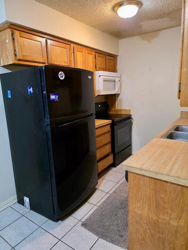 kitchen with light tile patterned floors, brown cabinets, light countertops, a textured ceiling, and black appliances