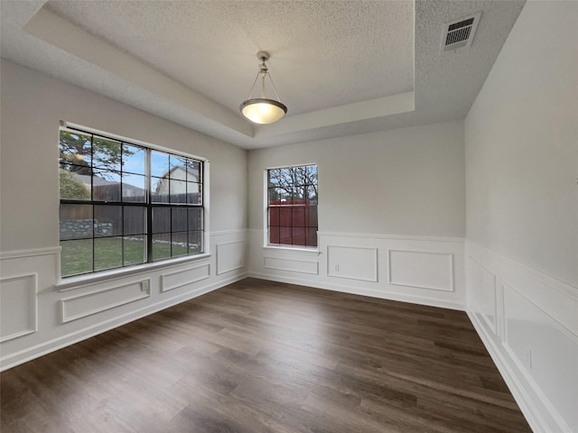 unfurnished dining area with dark wood-style floors, a textured ceiling, a raised ceiling, and visible vents