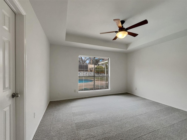 spare room with ceiling fan, carpet, a raised ceiling, and baseboards