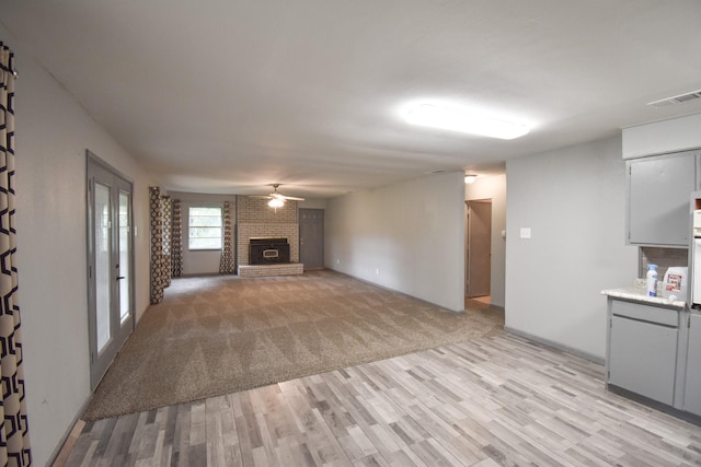408 Tarrapin, Murchison, TX 75778 - unfurnished living room with light colored carpet, visible vents, a brick fireplace, ceiling fan, and light wood-type flooring