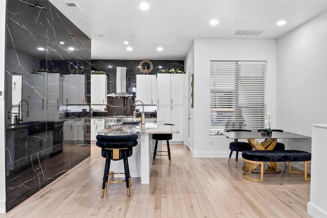 kitchen with visible vents, white cabinetry, a center island with sink, and wall chimney range hood