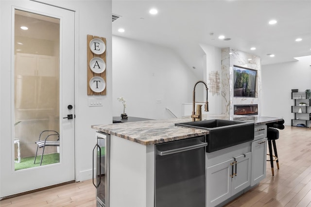 kitchen featuring wine cooler, a kitchen island with sink, light wood-style floors, a kitchen bar, and a sink