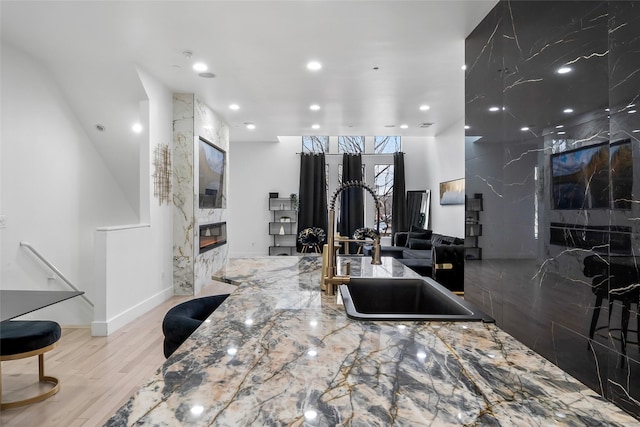 kitchen with a fireplace, recessed lighting, light wood-style flooring, a sink, and light stone countertops