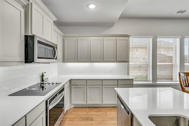 kitchen featuring appliances with stainless steel finishes, visible vents, light wood-style flooring, and decorative backsplash