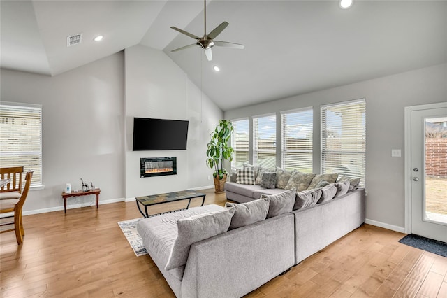 living room with light wood-style floors, a glass covered fireplace, visible vents, and plenty of natural light