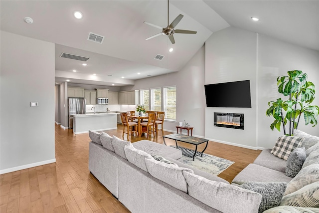 living area featuring light wood-style floors, a glass covered fireplace, and visible vents